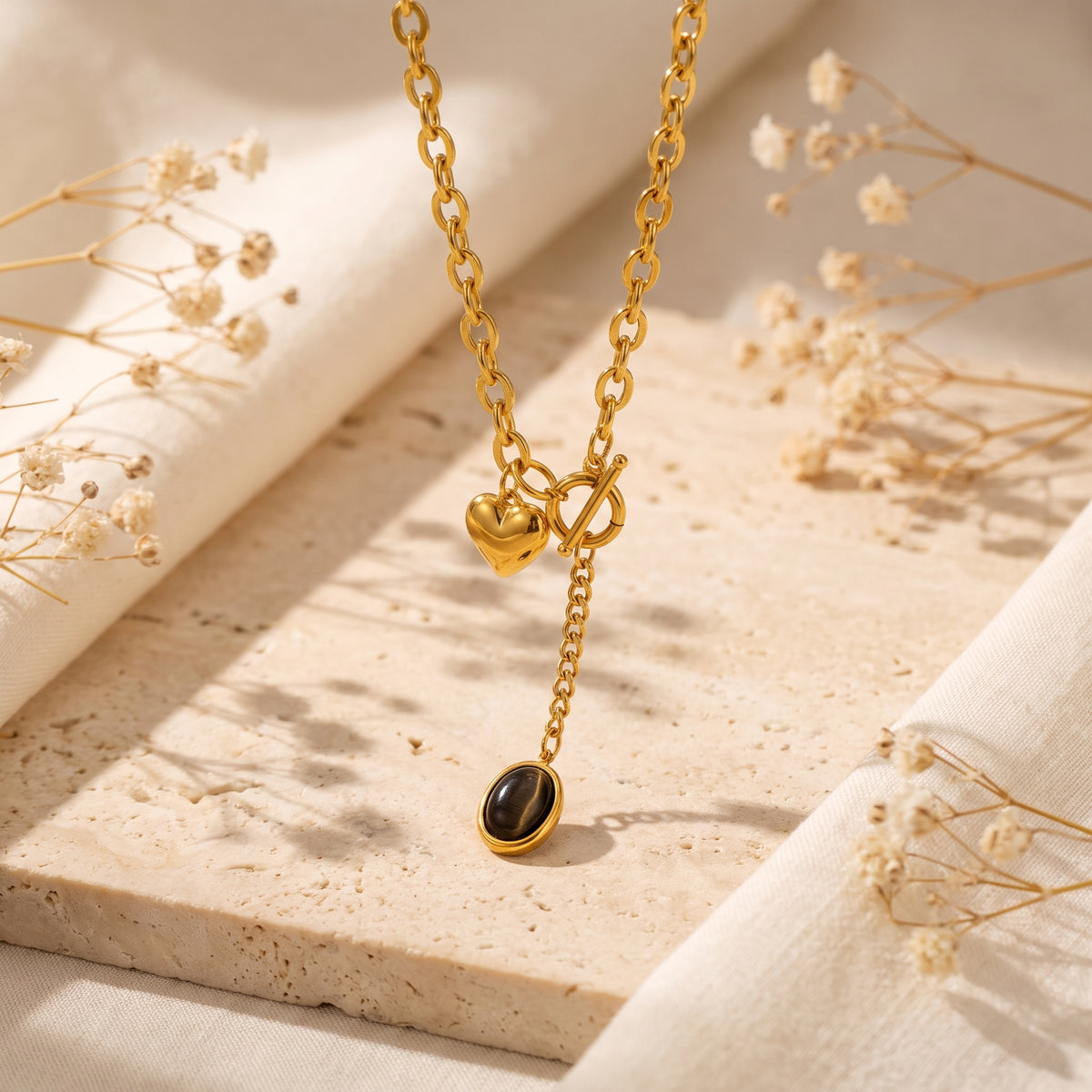 Close-up of the gold-tone toggle clasp, heart charm, and dark oval pendant hanging above a stone surface.