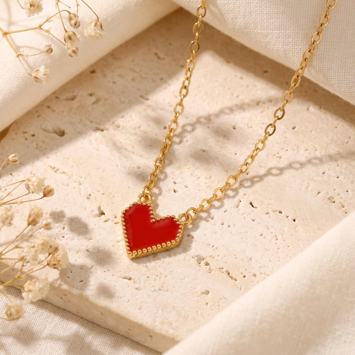 Flat lay of the red heart pendant with a beaded gold-tone border on a textured stone surface.