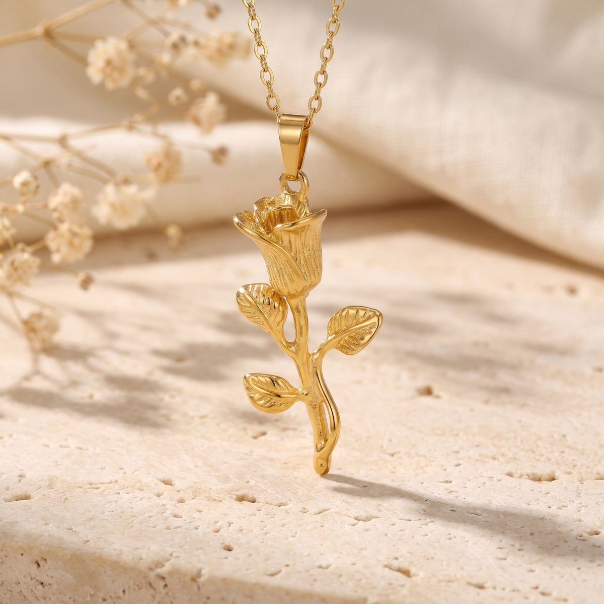 Close-up of the gold-tone rose pendant suspended vertically over a beige stone surface.