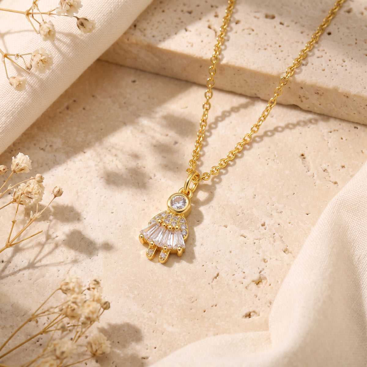 Angled view of the gold-tone girl pendant with round and elongated clear simulated diamond accents on a stone surface.