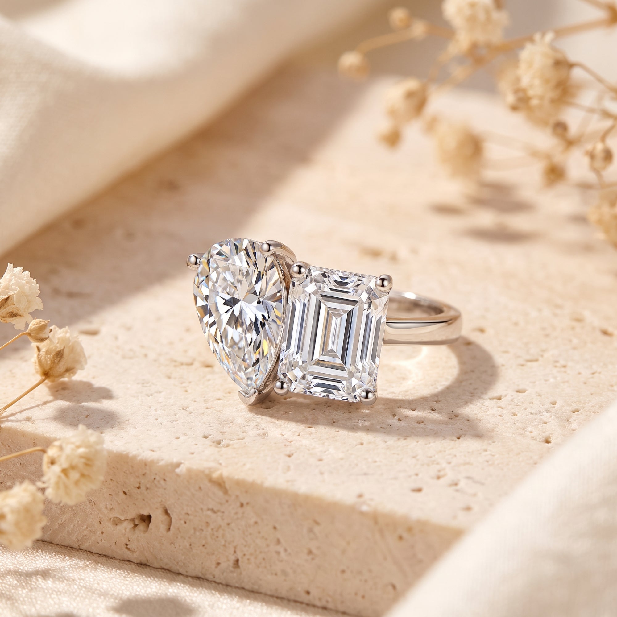 Close-up side view of a sterling silver bypass ring with pear and emerald cut simulated diamonds on a stone base.