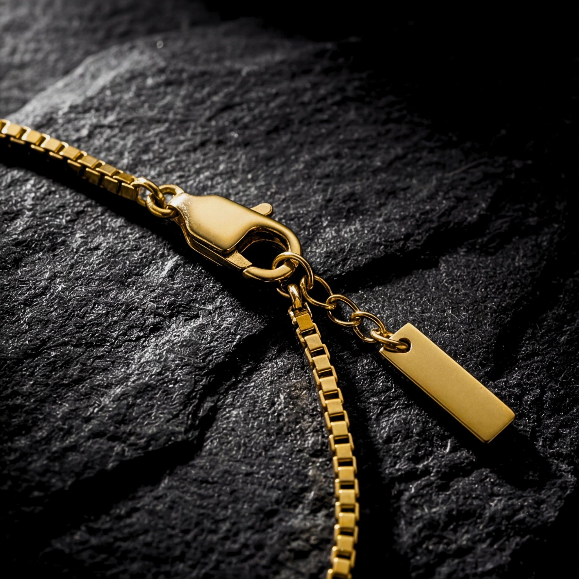 Close-up of the lobster clasp and gold stainless steel box chain links on a dark stone surface.