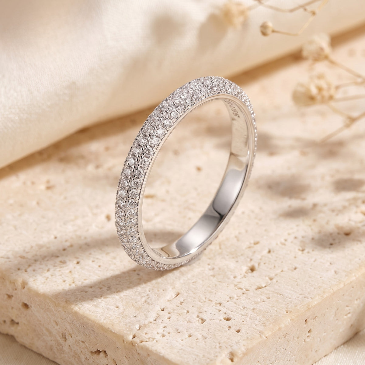 Three-row micro-pavé silver band ring standing upright on a beige stone surface.