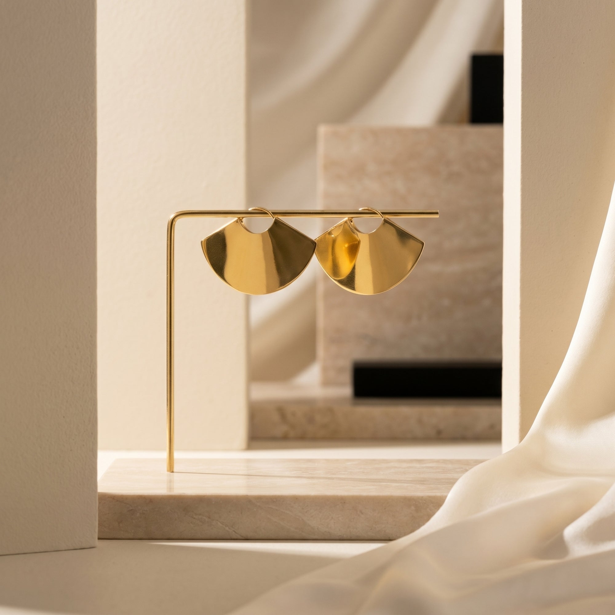 Gold fan earrings in 18K gold PVD stainless steel on a minimalist display stand.