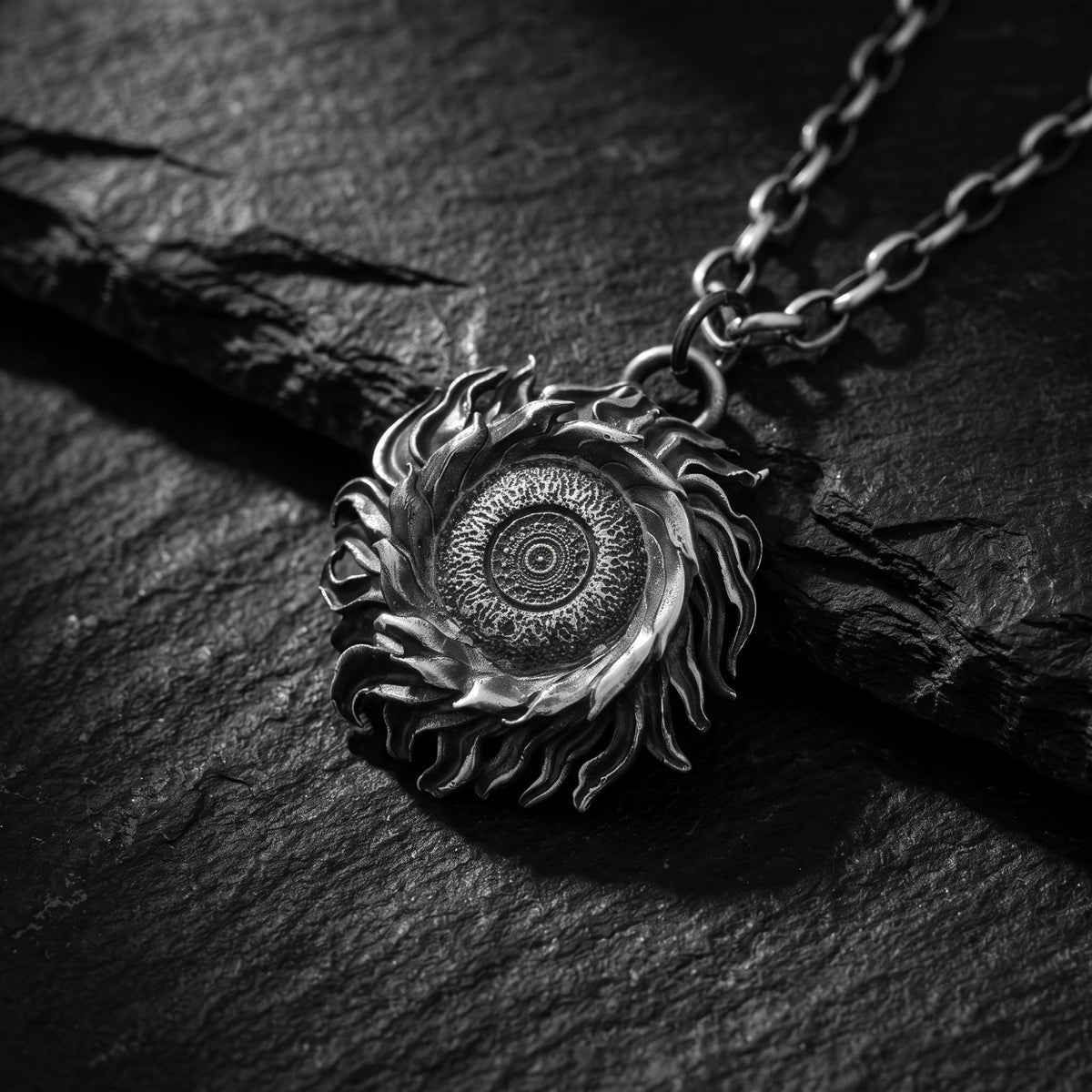 Angled close-up of the silver solar flare medallion pendant lying on a dark stone surface.