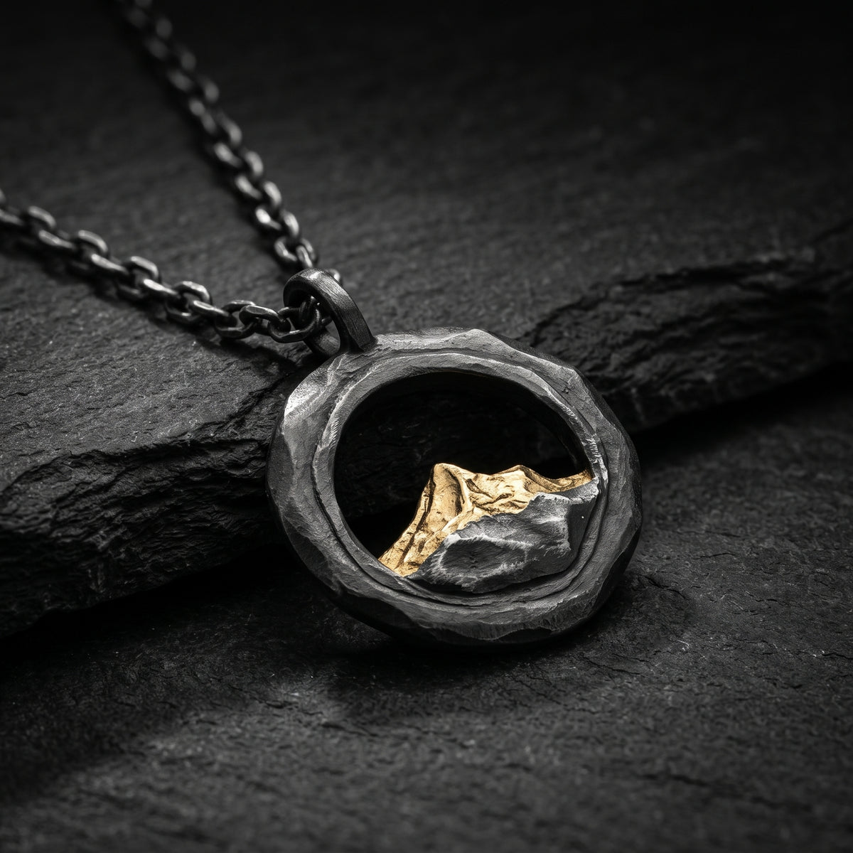Close-up angled view of the textured circular silver pendant with a gold-tone mountain peak on dark stone.