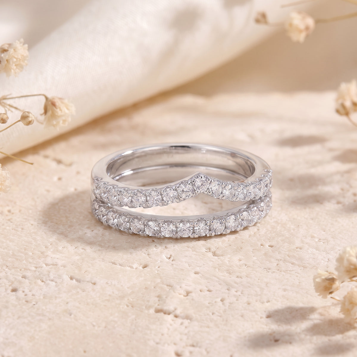 Front view of the silver double chevron ring set lined with clear cubic zirconia on a stone surface.