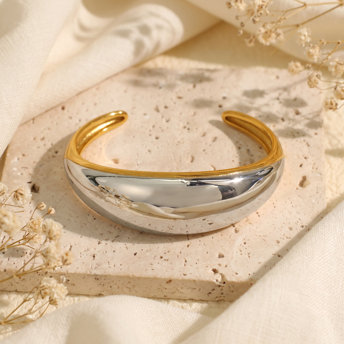 Front view of the two-tone dome cuff bracelet on a beige stone slab, showing the polished silver dome and gold inner rim.