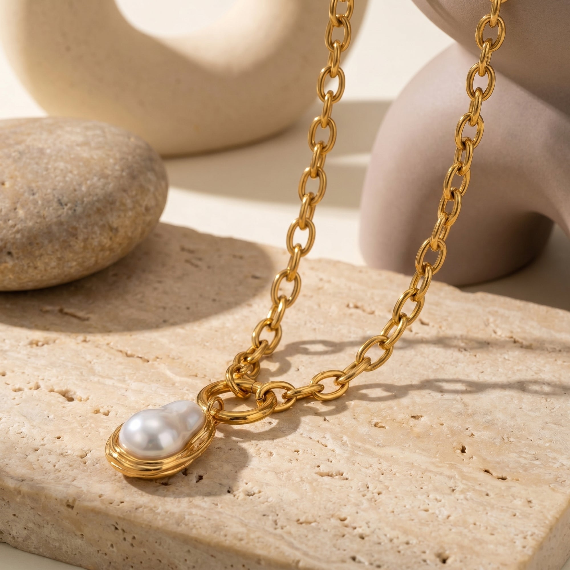Close-up of the gold link chain and irregular synthetic pearl pendant on a textured stone.