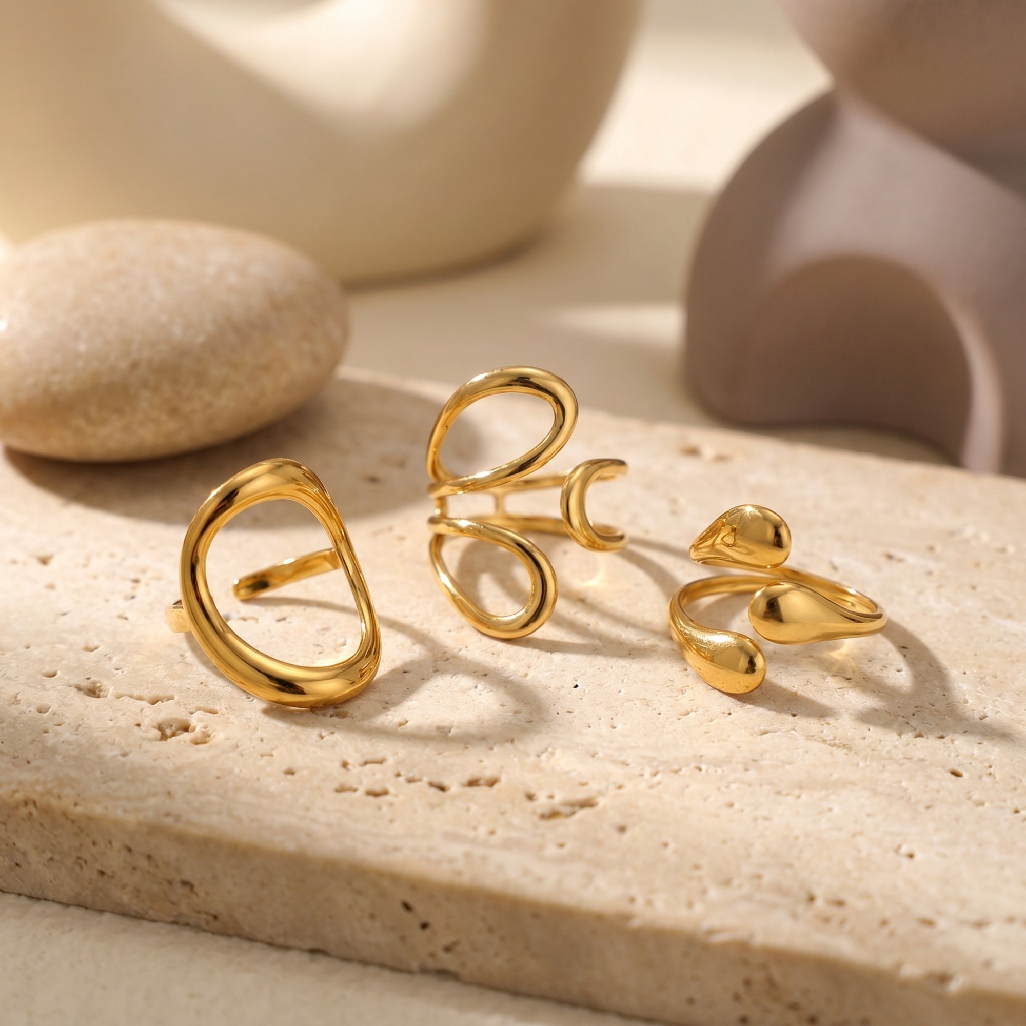Trio of organic gold stainless steel rings displayed on a textured stone slab.