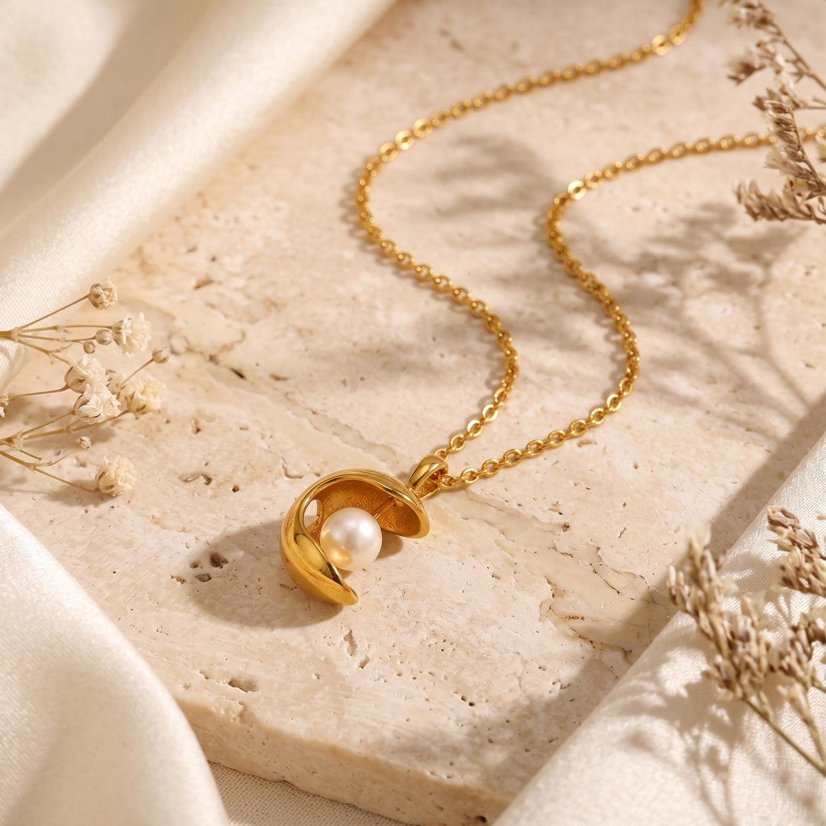Flat lay of the gold-tone crescent pearl necklace on a textured stone surface with draped fabric.