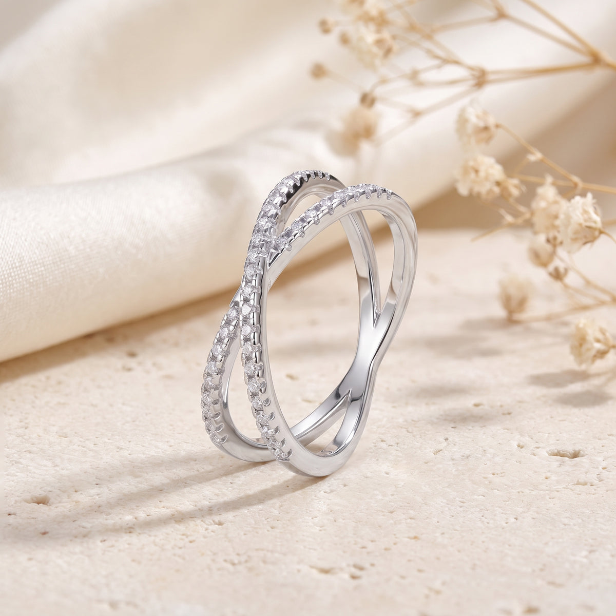 Silver crossover ring standing upright on a textured stone block, showing its interlocking bands.