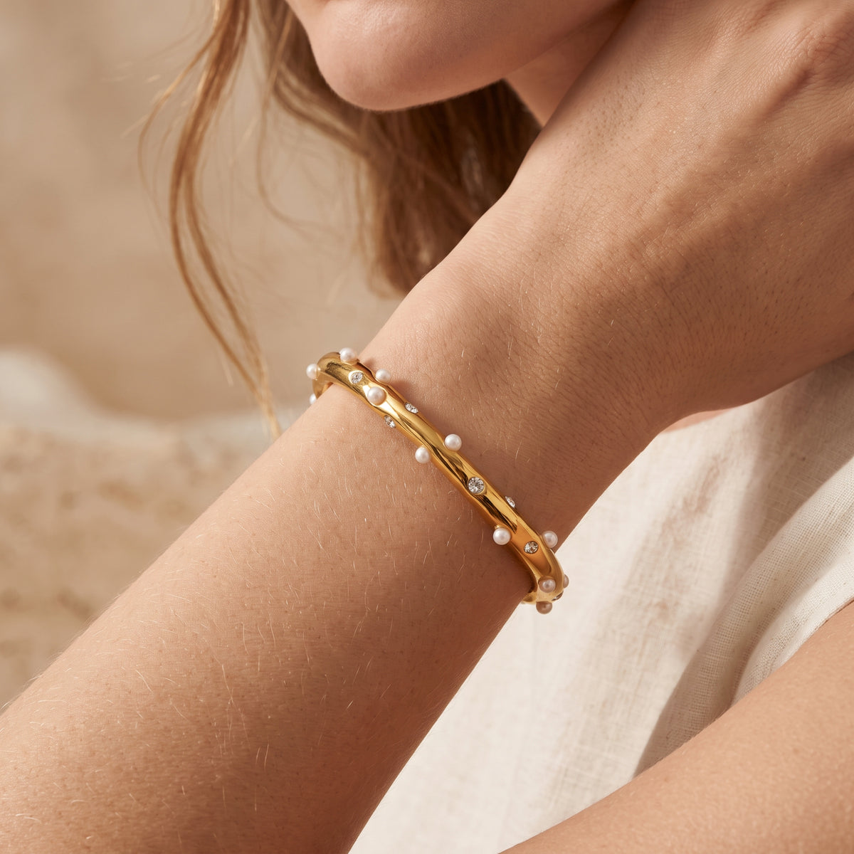 Lifestyle view of a gold-tone pearl and cubic zirconia open cuff bracelet worn on a person's wrist.