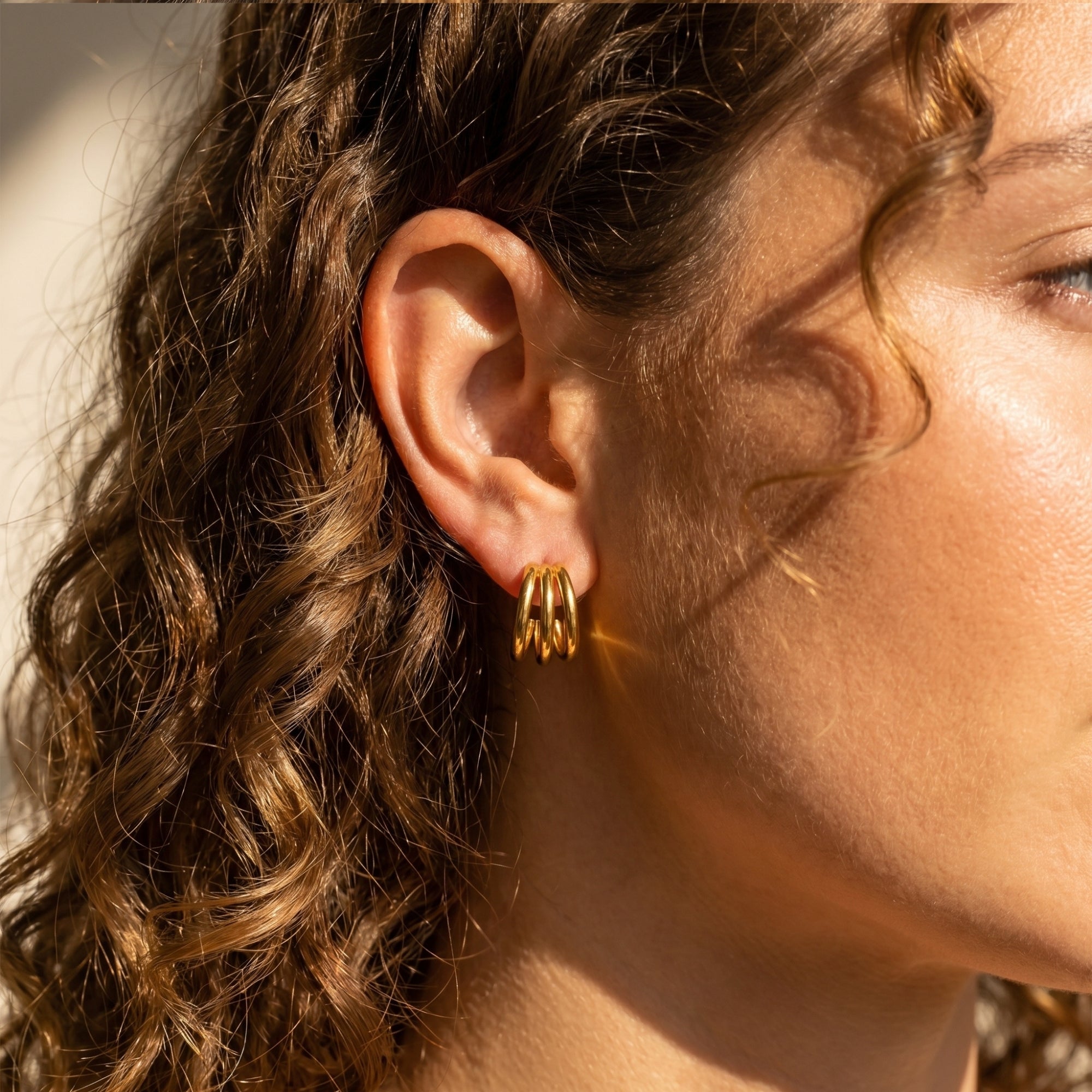 Model wearing gold triple-band hoop earrings in a side profile view.