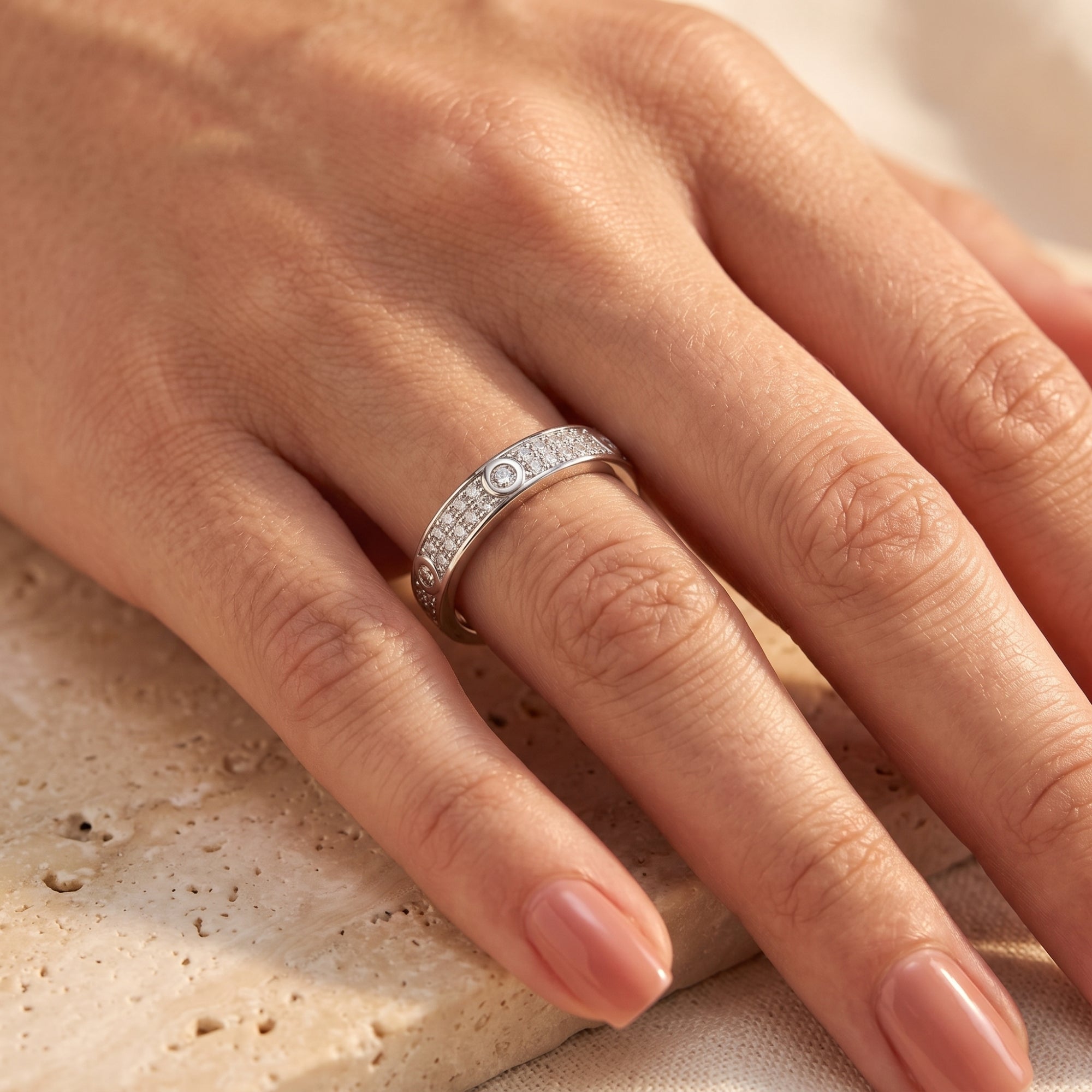 Silver pavé CZ ring shown on a hand resting on a textured stone surface.