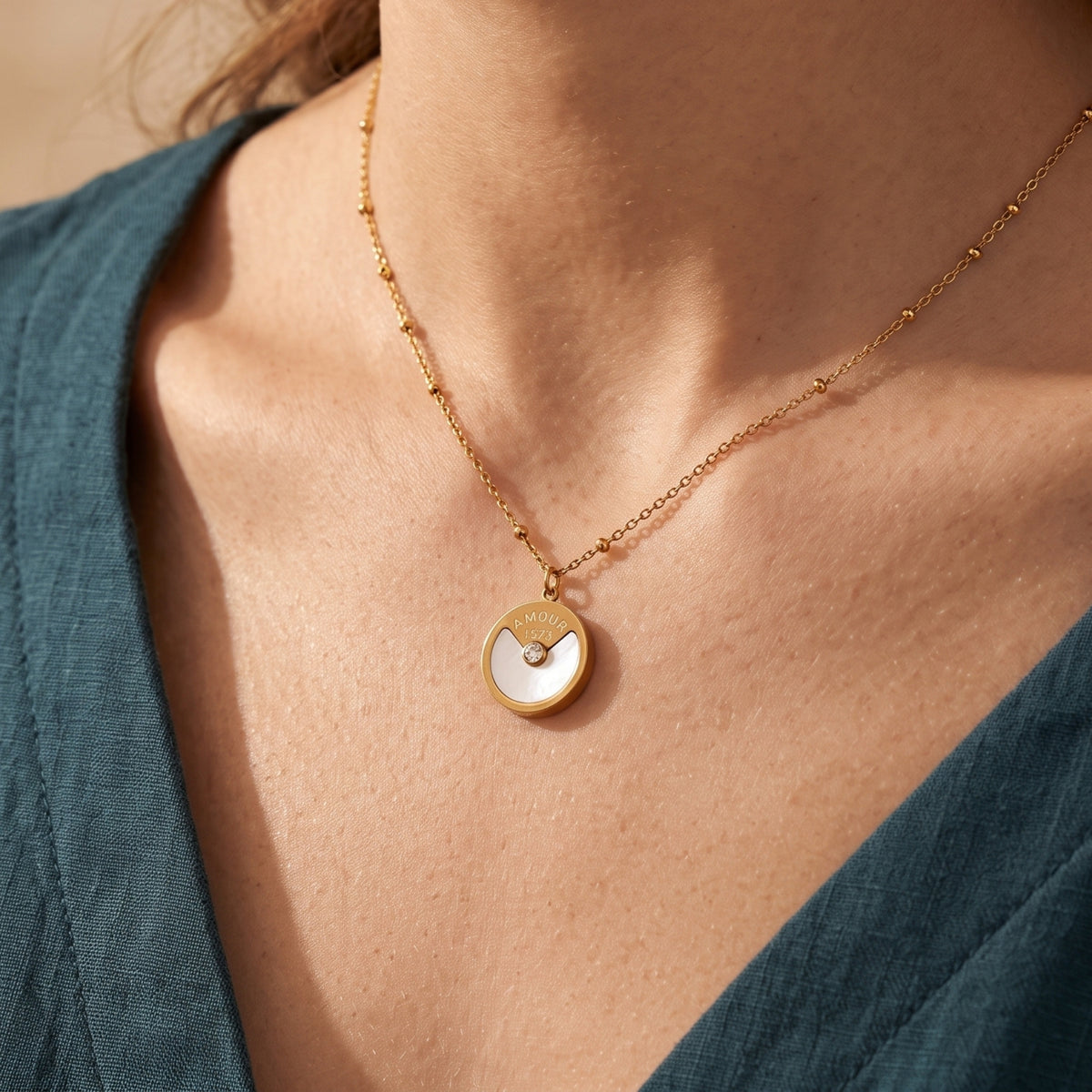 Gold L'Amour pendant necklace with mother-of-pearl inlay worn by a model in a teal dress.