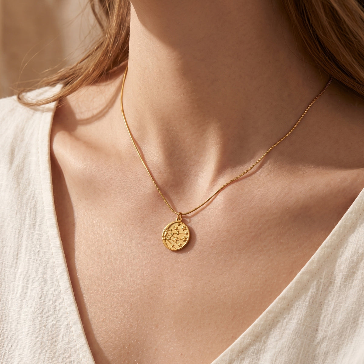 18K gold celestial medallion necklace worn by a model in a white top.