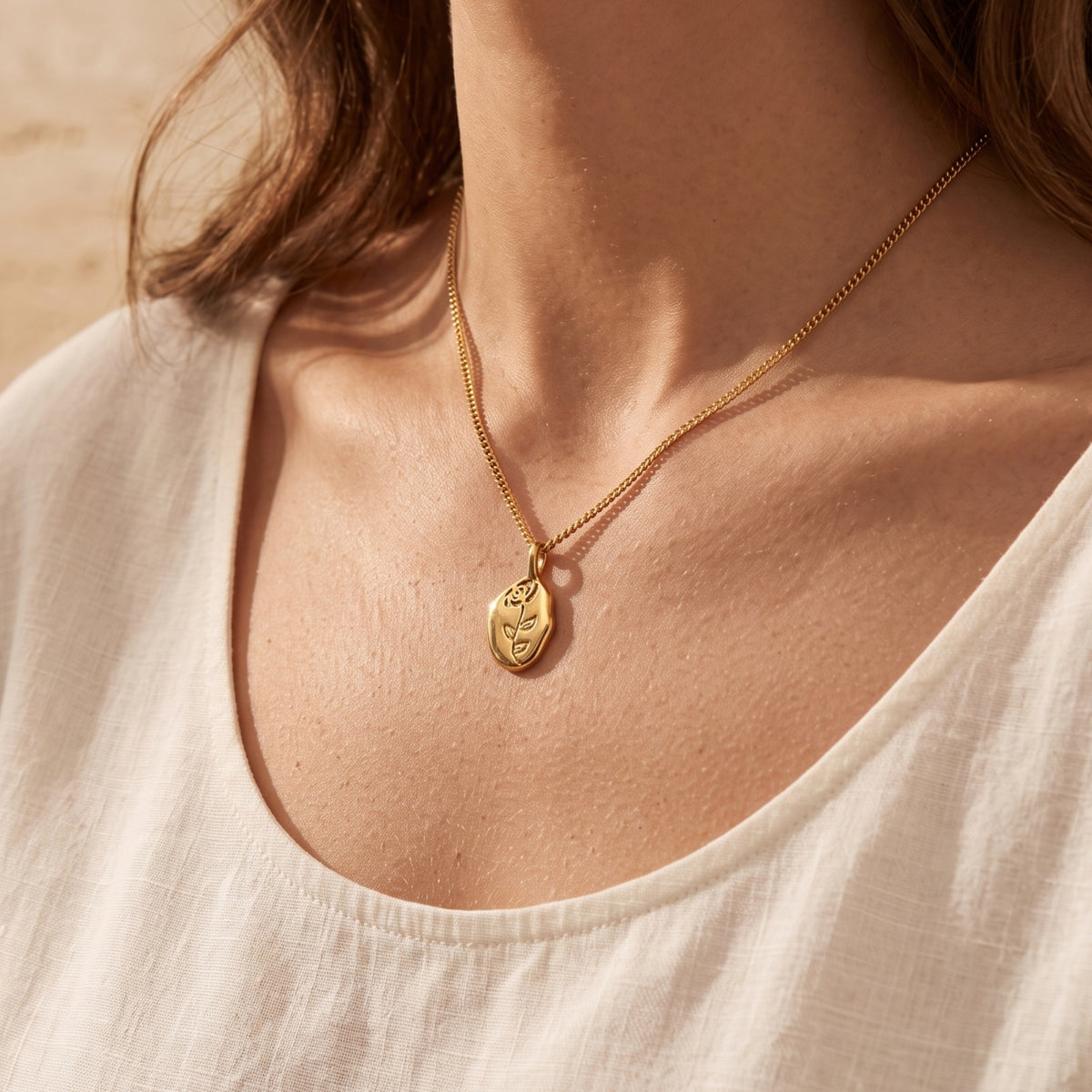 Lifestyle view of a woman wearing the gold stainless steel rose pendant necklace with a white linen top.