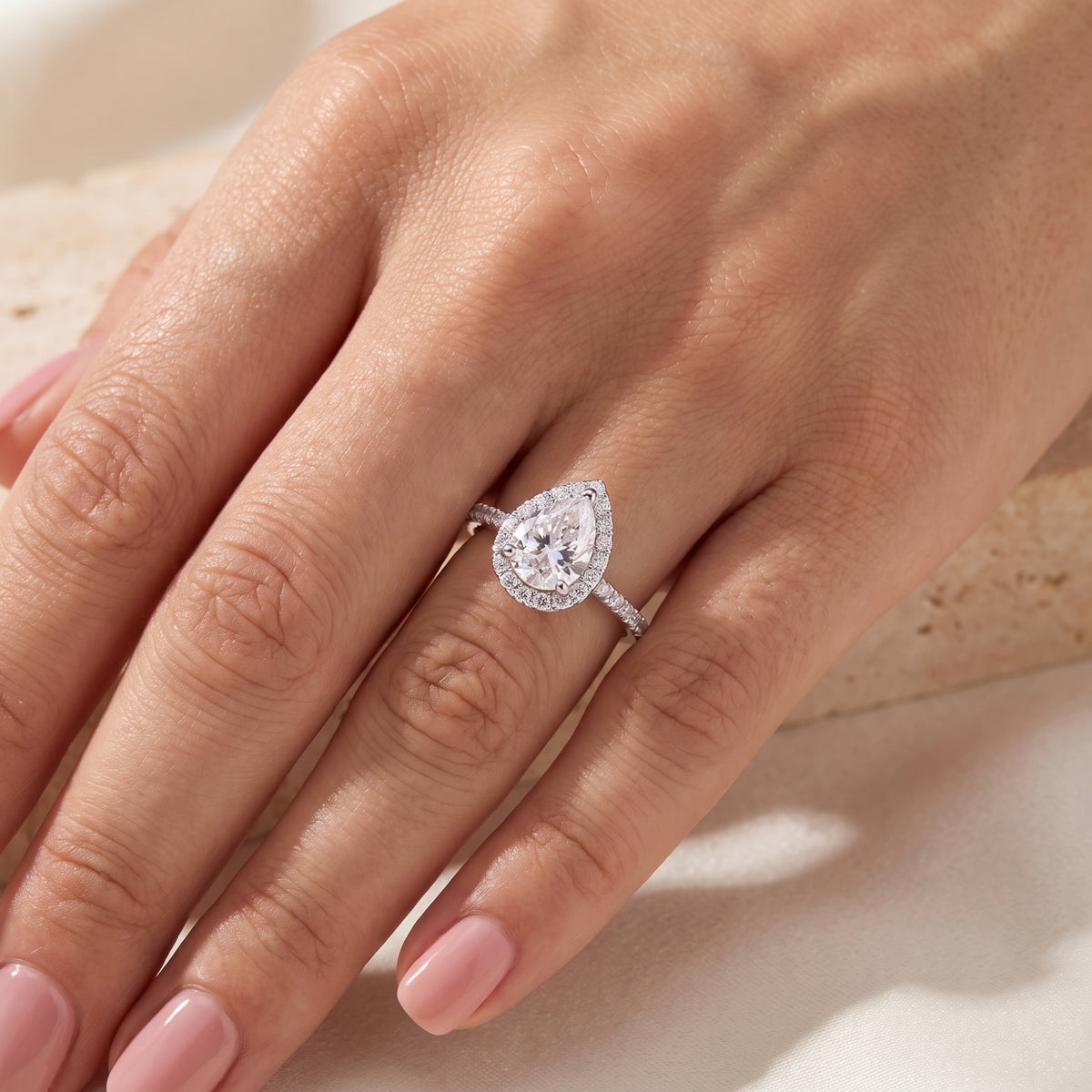 Overhead view of a hand displaying the pear-cut halo ring set on a silver pavé band.