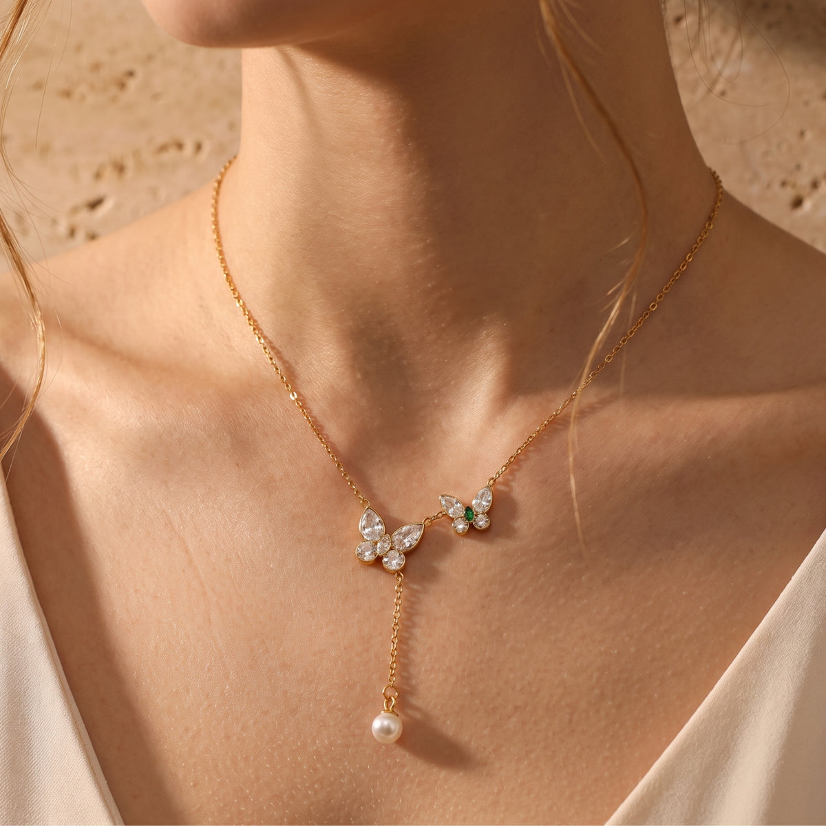 Front view of a model wearing a gold-tone butterfly lariat necklace with clear stones and a dangling pearl.