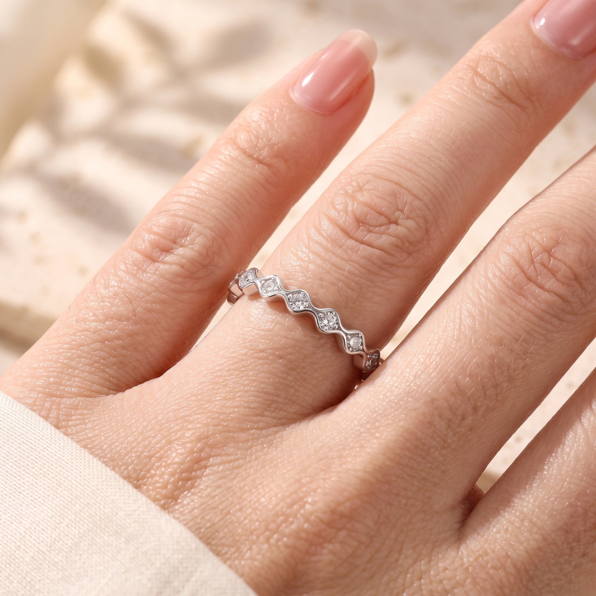 Detailed view of the Evangeline wavy silver ring with simulated diamonds on a hand.