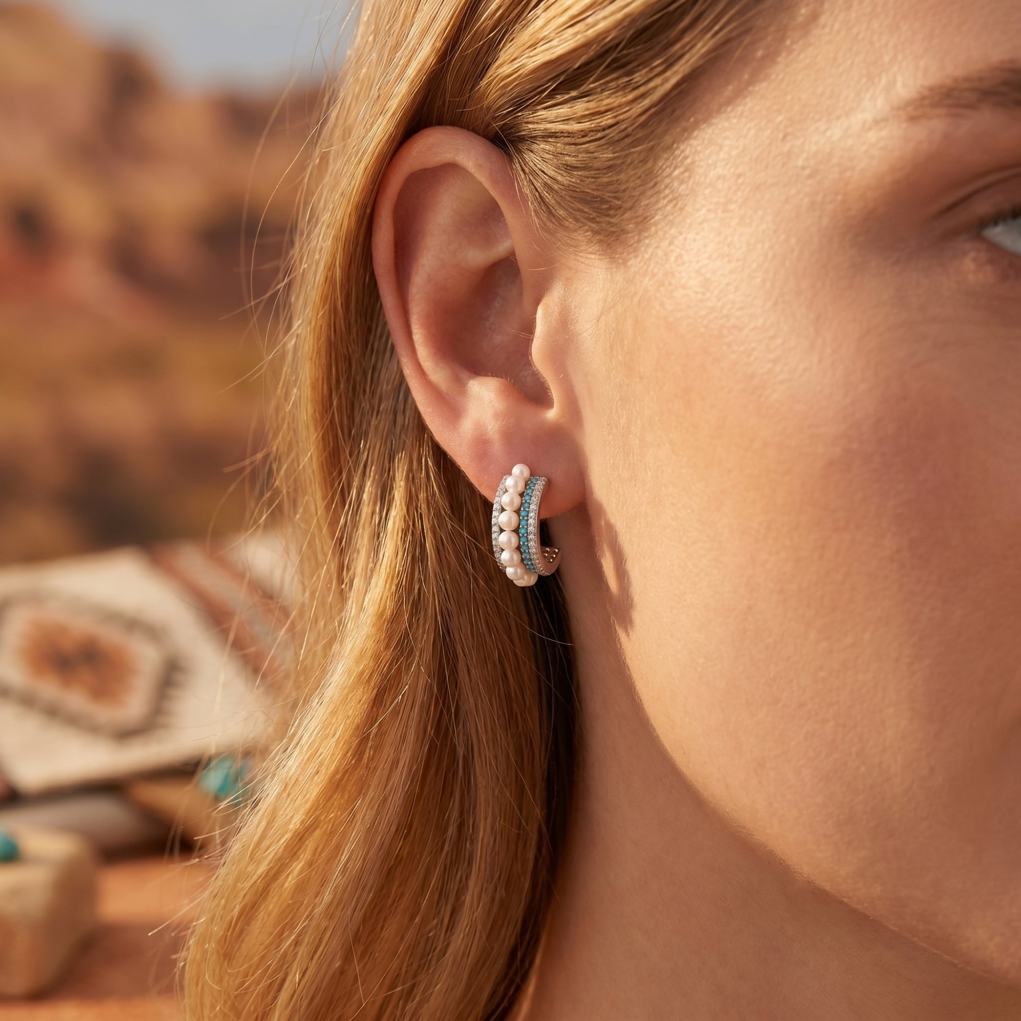 Model wearing silver turquoise and pearl C-hoop earrings against a blurred desert landscape.