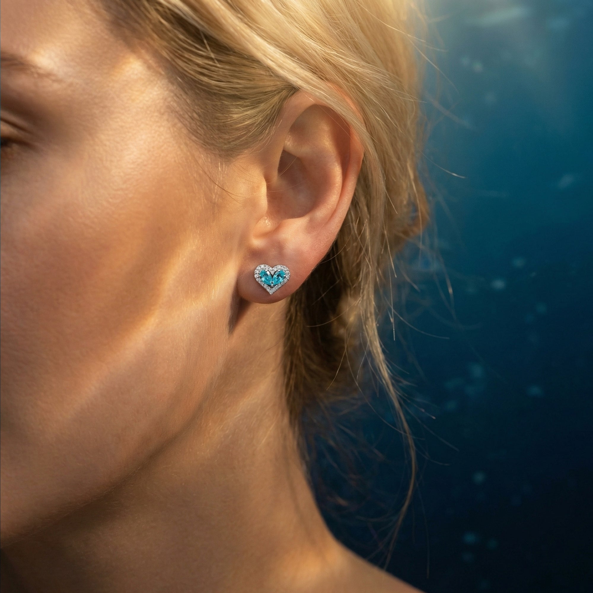 Close-up of a heart-shaped pear-cut aquamarine and diamond halo earring worn on a woman's ear.
