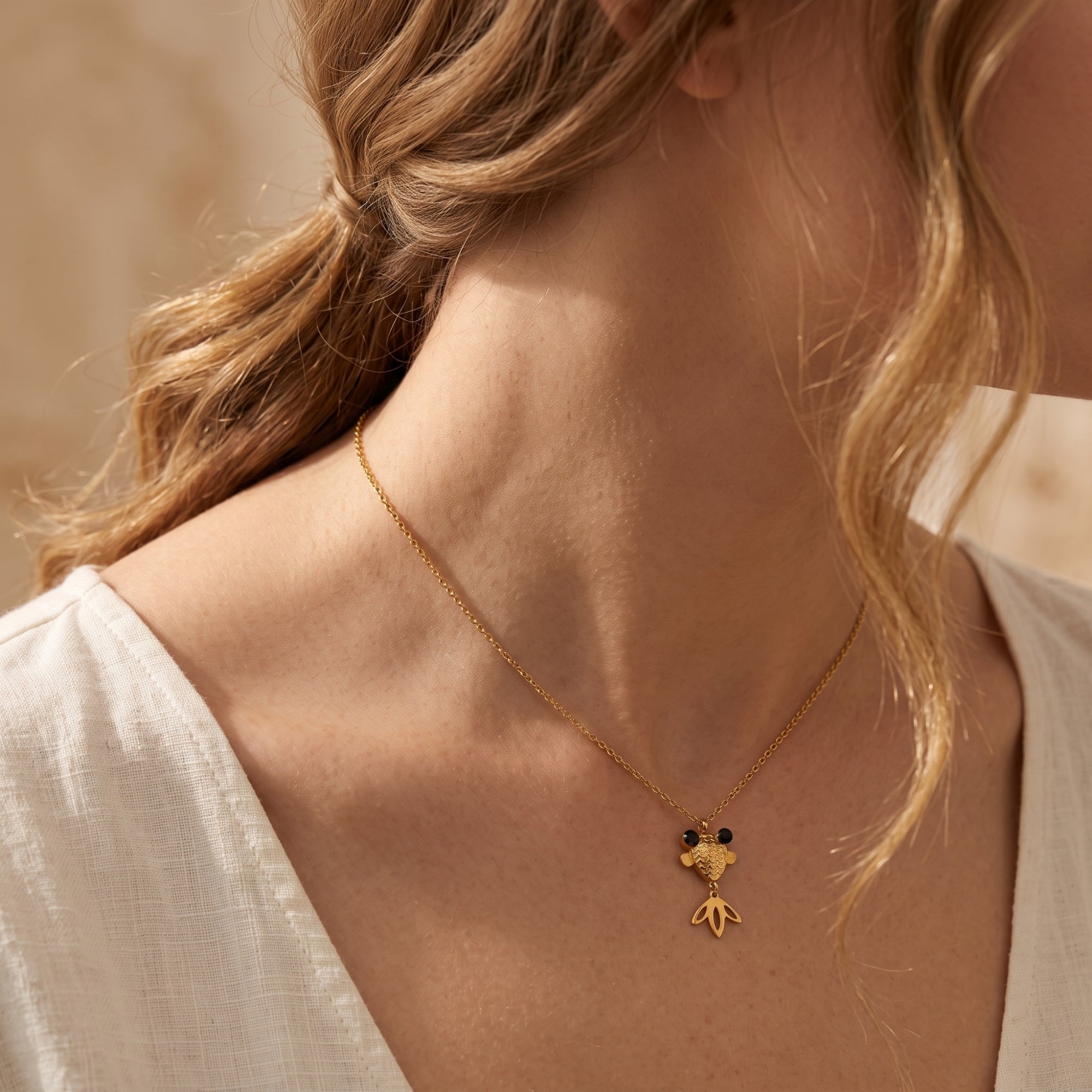 Model wearing a gold finish goldfish pendant necklace with a white linen shirt.