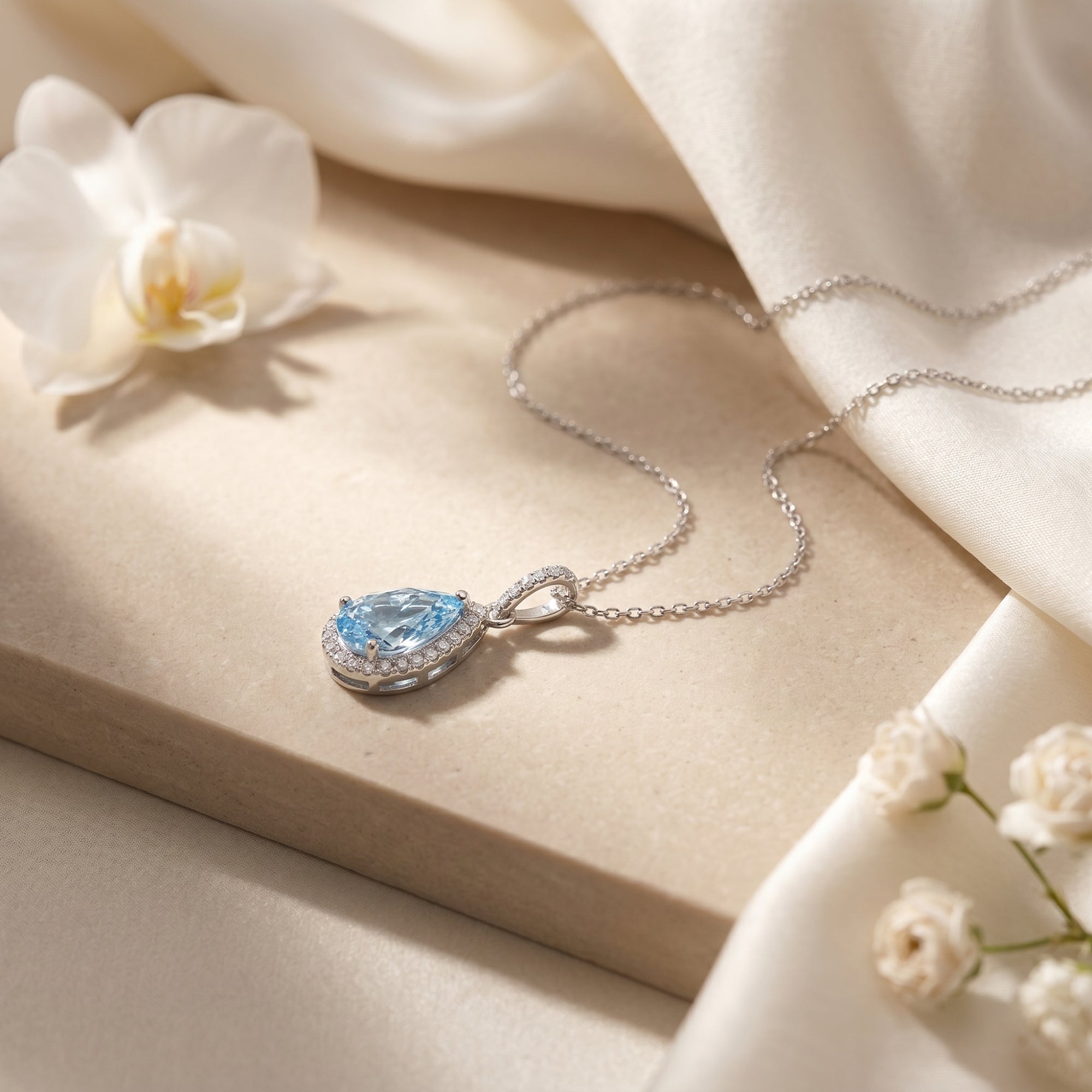 Close-up side view of the pear-cut aquamarine halo pendant in sterling silver on a stone surface.