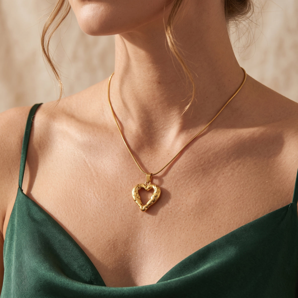 Model wearing the gold-tone molten heart pendant necklace paired with a green satin top.