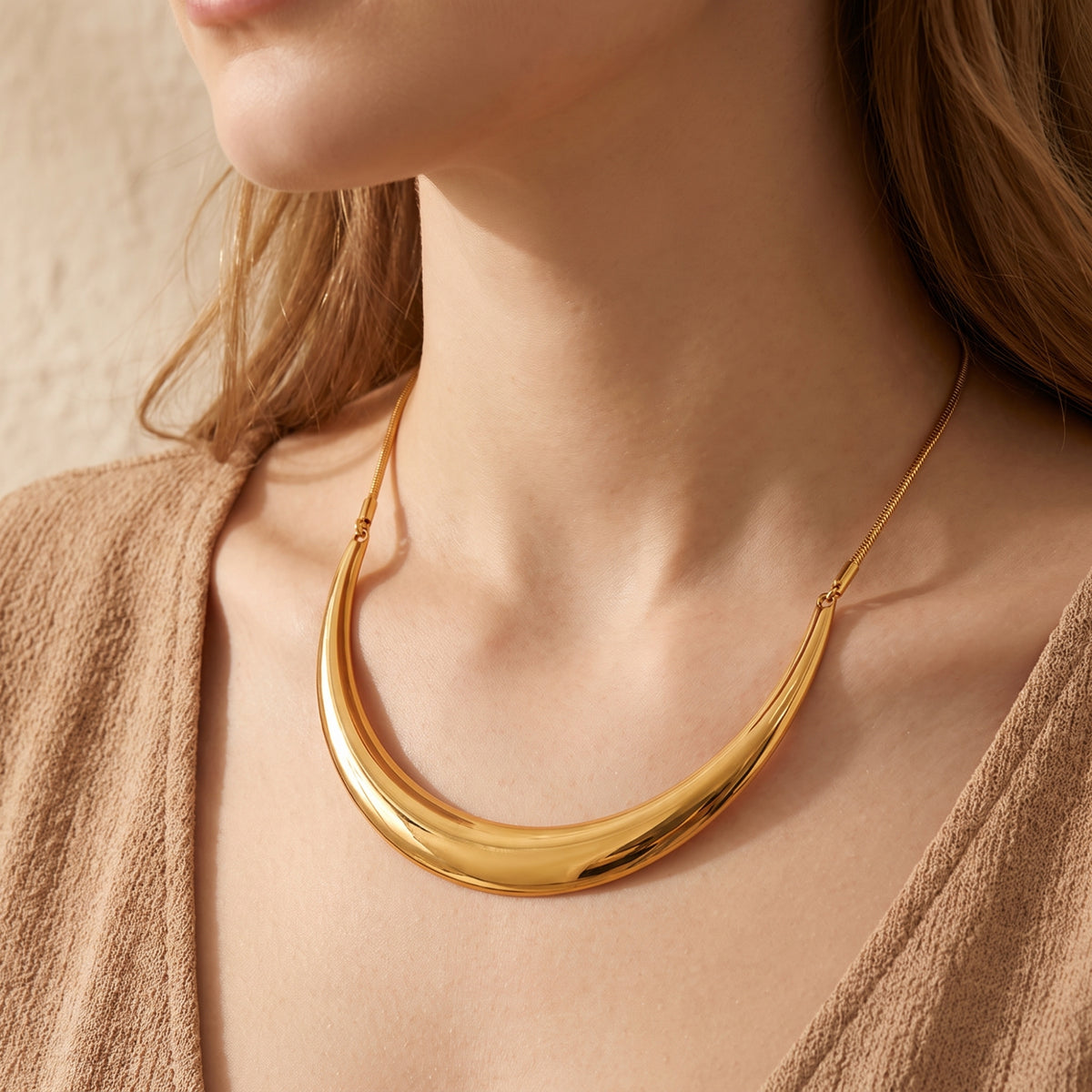 Model wearing the smooth gold-tone crescent collar necklace with a beige textured open cardigan.