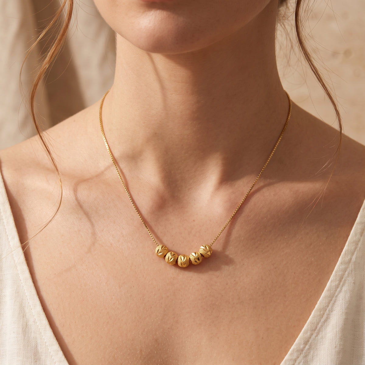 Wider view of a model wearing the gold-tone necklace, with five carved beads resting along her collarbone.