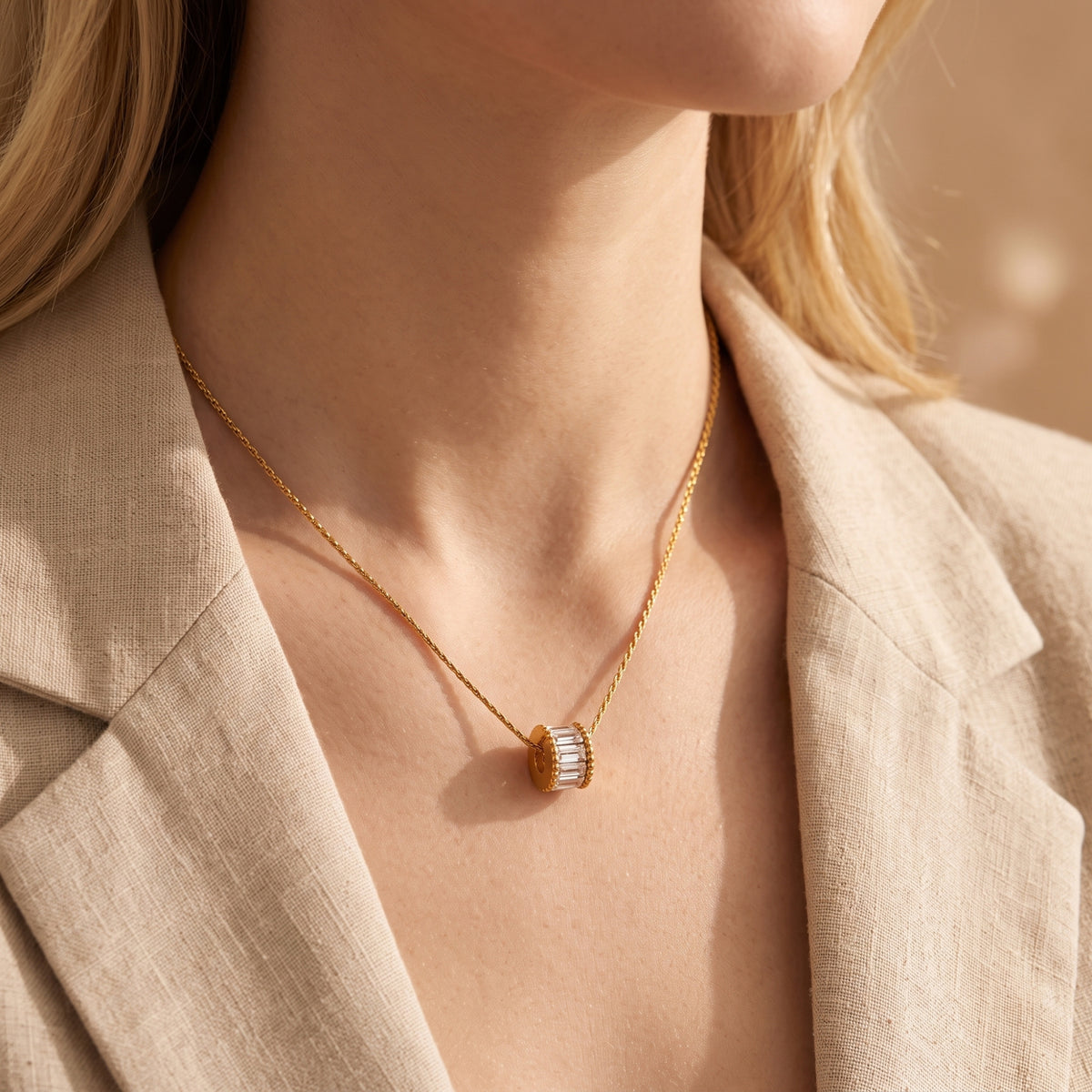 Gold statement necklace with a baguette-cut stone pendant worn by a model in a beige blazer.