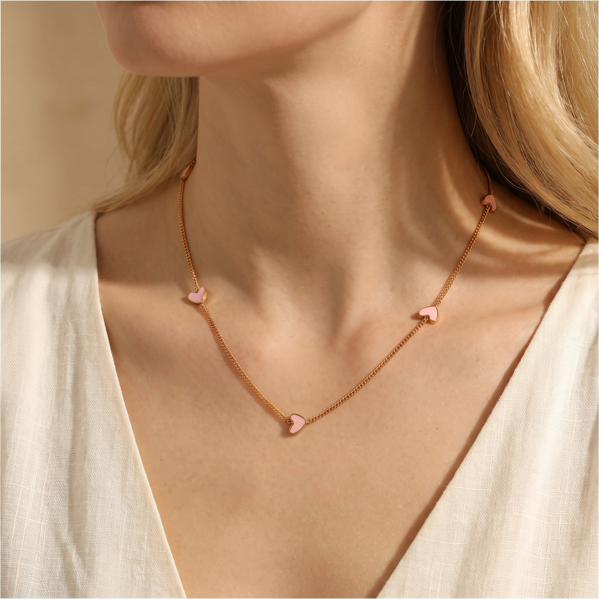 Close view of a gold-tone necklace with pink enamel heart stations worn over a white top.