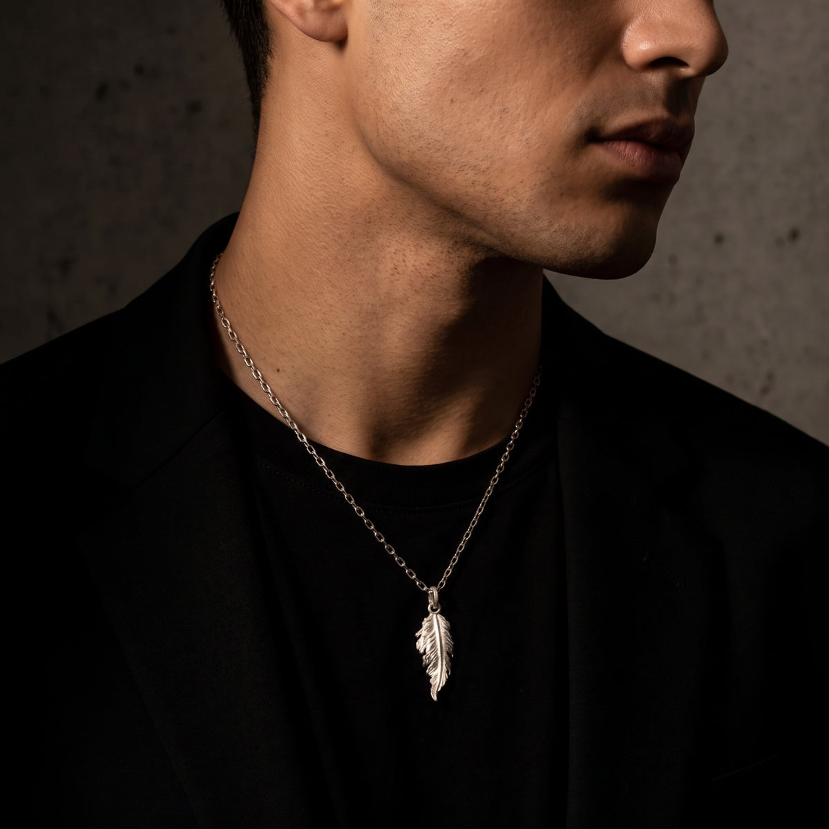 Side profile view of a man wearing the silver feather pendant necklace with a black blazer.