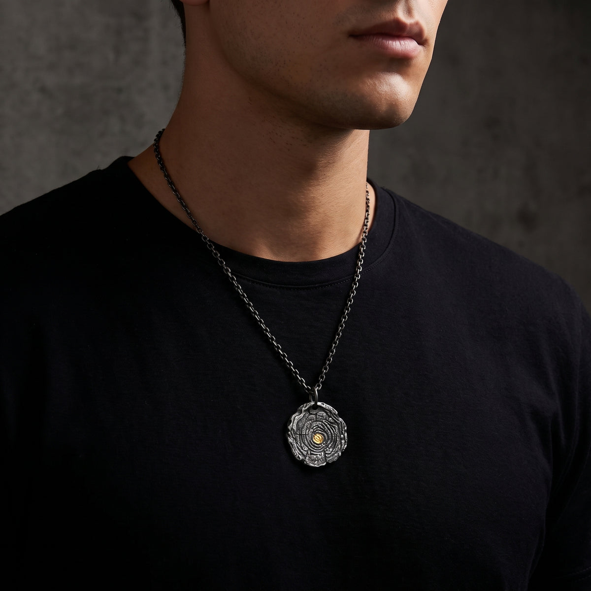 Man wearing the silver growth ring pendant necklace over a black crewneck T-shirt.