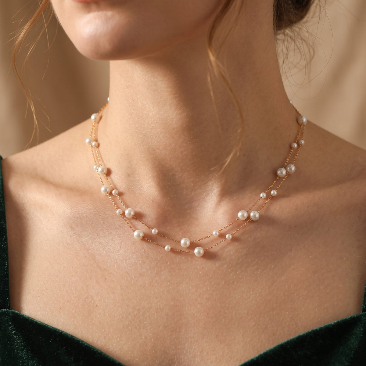 Model wearing the double-strand gold-tone pearl station necklace over a dark green velvet top.