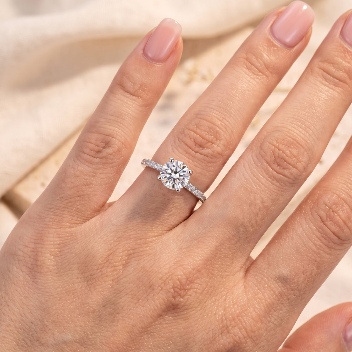 Silver round-cut accent ring worn on a finger, shown from above against a light neutral background.