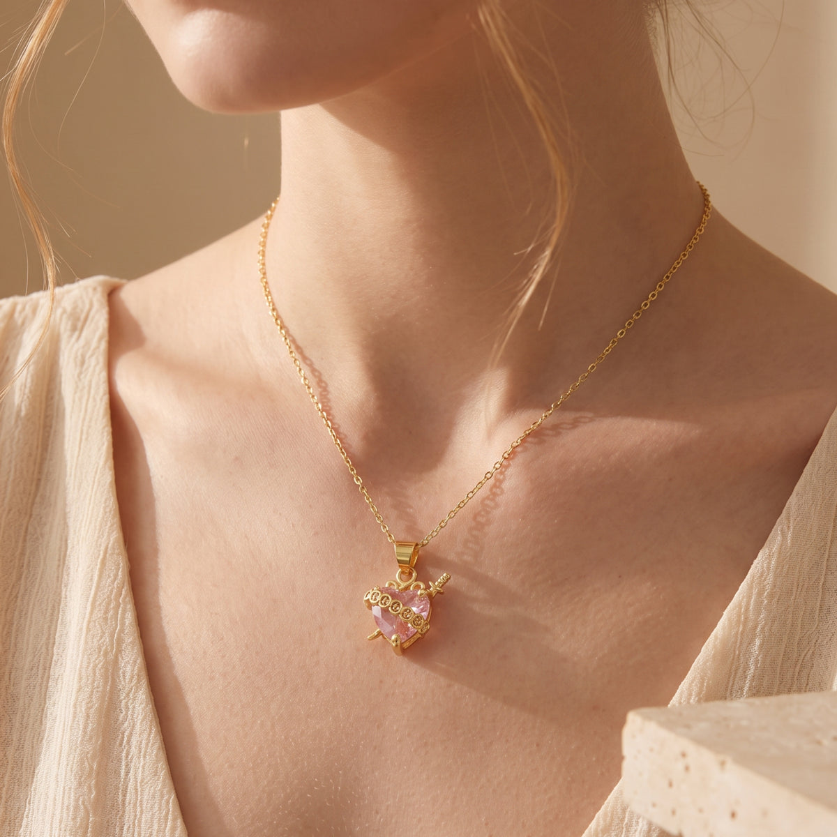 Frontal view of a model wearing the gold-tone pendant necklace with a pink heart crystal.