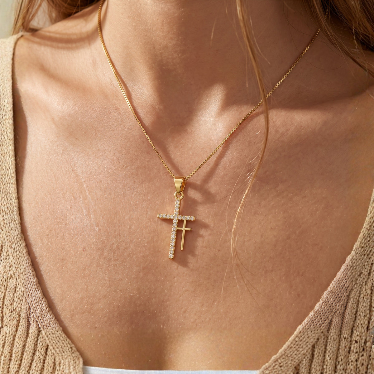 Close-up of the gold-tone double cross pendant necklace worn with a beige ribbed top