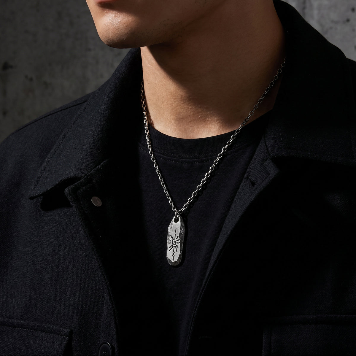 Model wearing the silver pendant necklace over a black shirt with an open dark jacket.