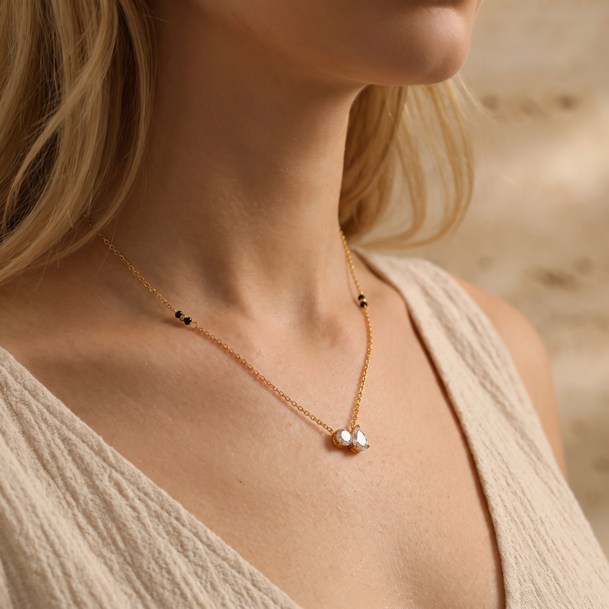 Side-angle view of a model wearing the gold-tone duo pendant necklace with round and pear-cut clear stones.