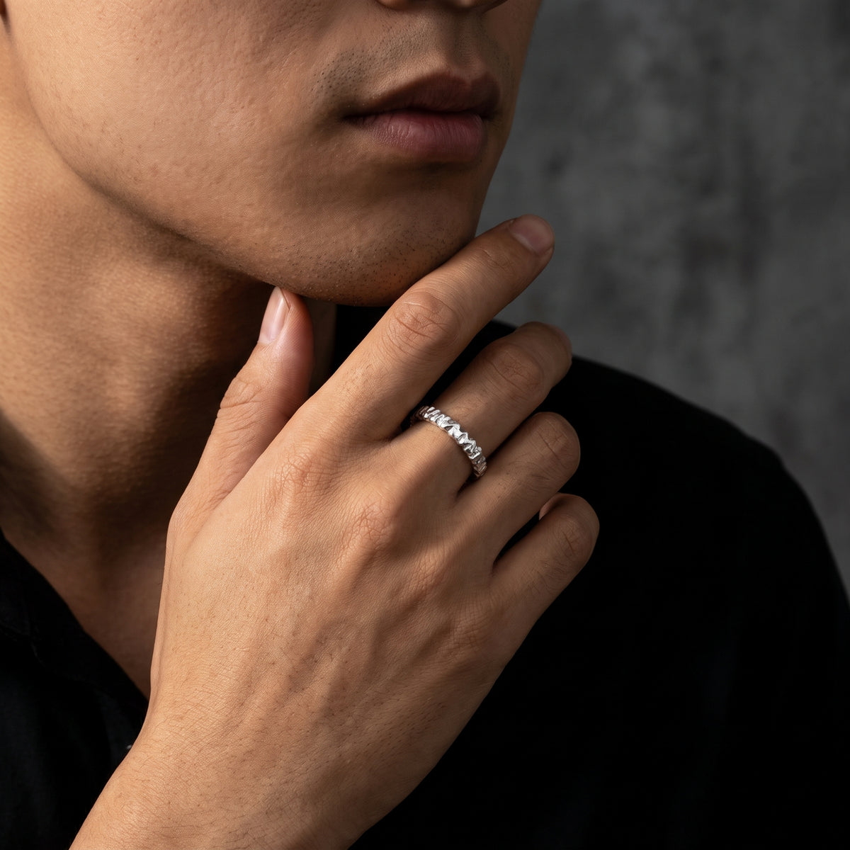 Model resting a hand near his chin while wearing a carved silver open-band ring on his ring finger.