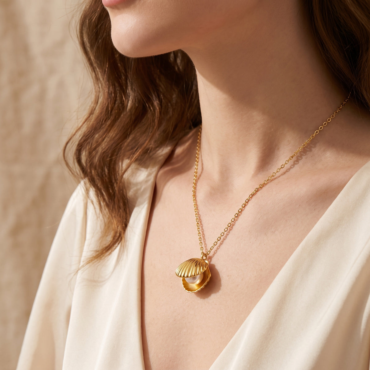 Model wearing the gold-tone shell pendant with a white pearl over a light open-neck garment.