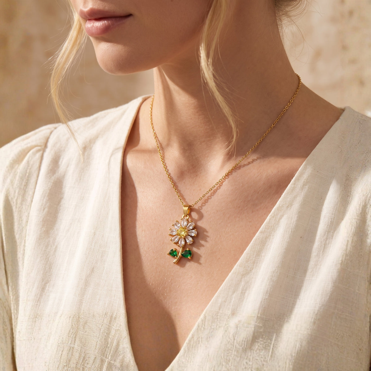 Wider view of a model wearing the gold-tone daisy pendant necklace with a white V-neck top.