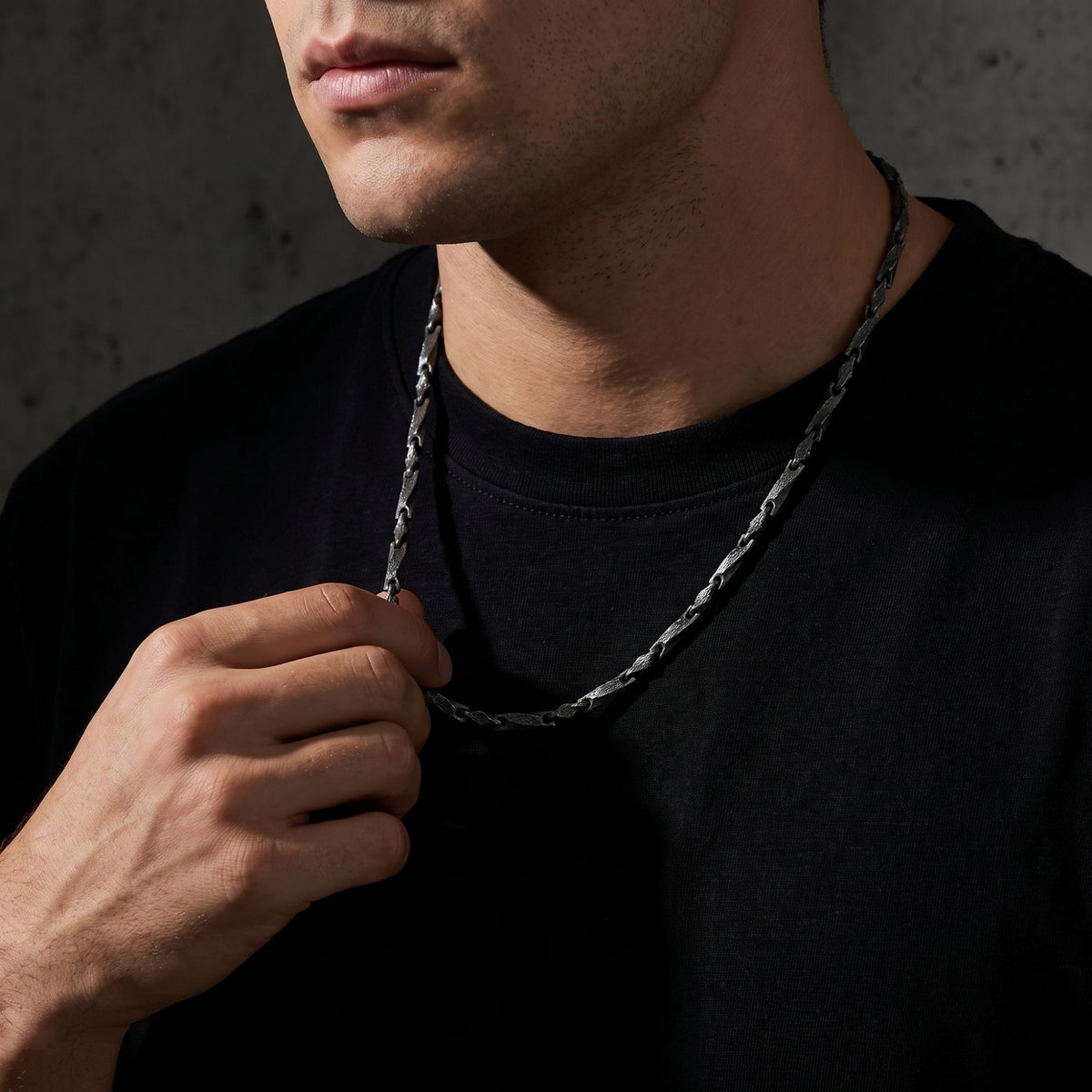 Man wearing the textured silver bar link chain over a black T-shirt while holding its front section.