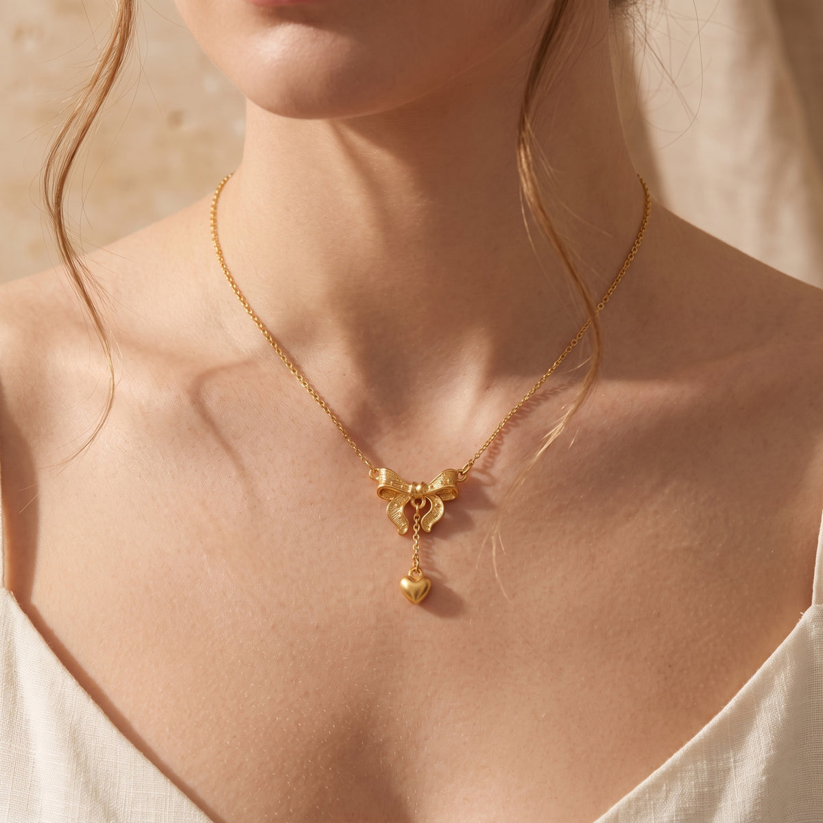 Close-up of a model wearing the gold-tone bow and heart pendant necklace, with loose hair framing the chest.