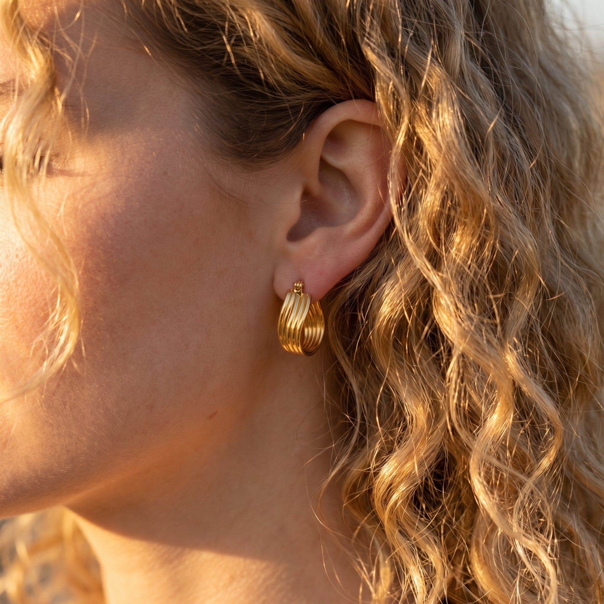 Side profile of a model wearing gold multi-row hoop earrings.