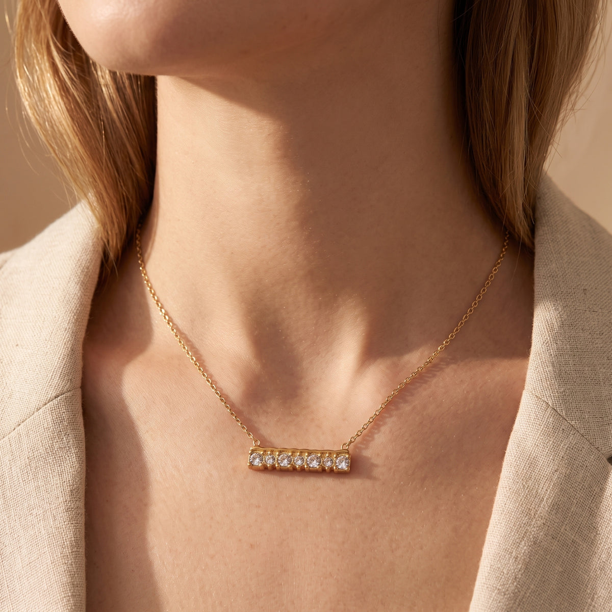 The Aurendelle gold bar necklace with seven cubic zirconia stones worn by a model over a beige linen blazer.
