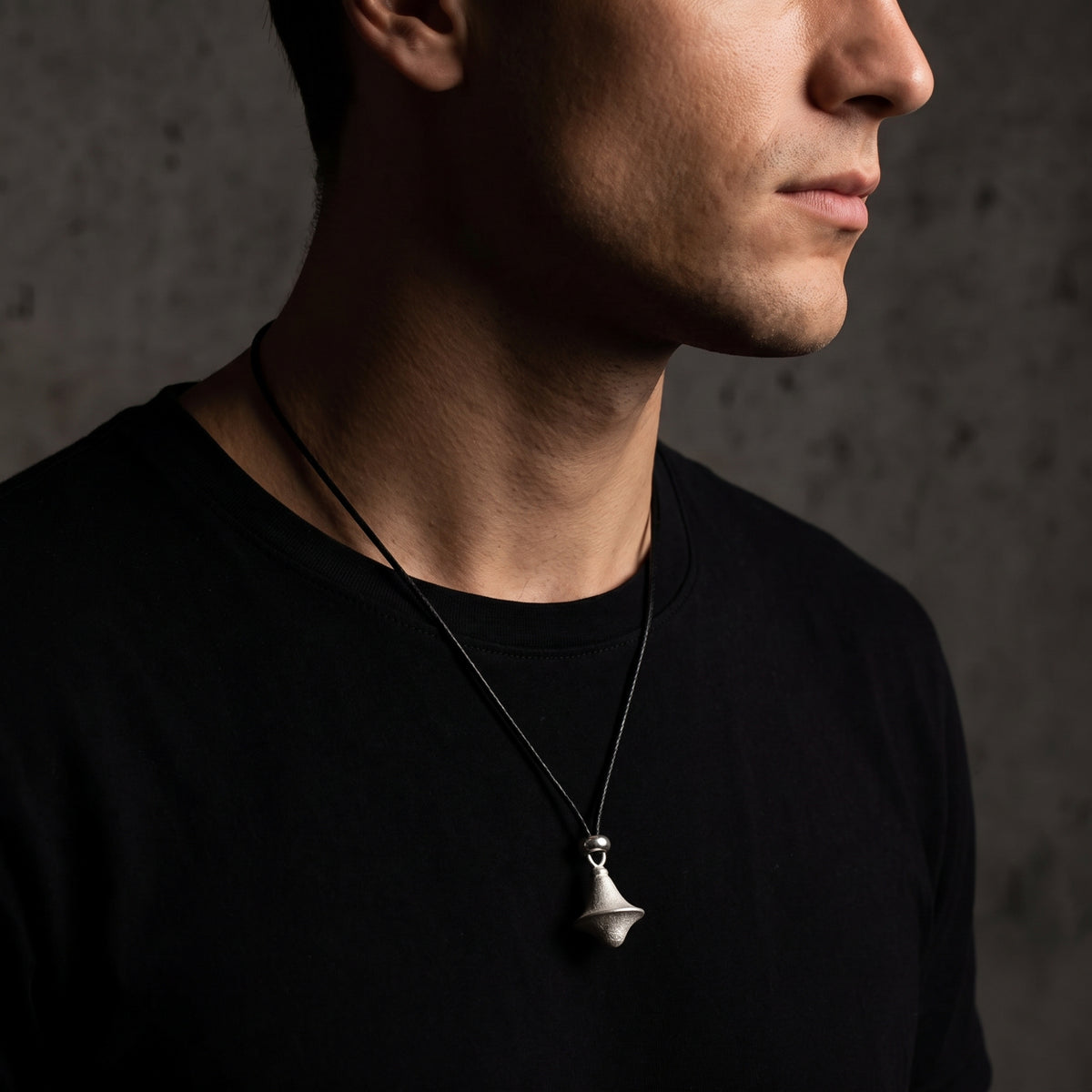 Three-quarter view of a person wearing the textured silver double-cone pendant on a black cord over a black T-shirt.
